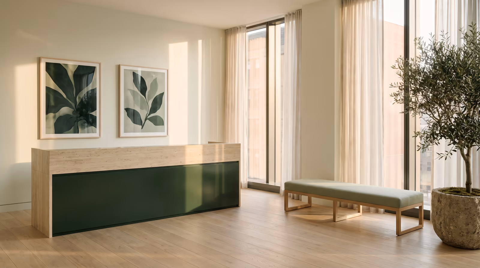 Visualization of the arrival space: a travertine reception desk with a deep green front, framed botanical prints, and an olive tree in warm daylight