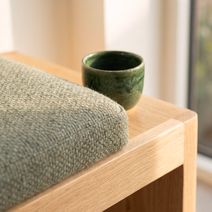 Rendering of a waiting area detail: sage wool upholstery on an oak bench with a green glazed cup